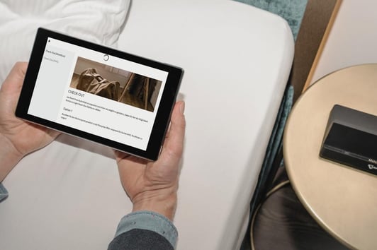 SuitePad-Tablets im Zimmer, die von einem Gast in einem Hotelzimmer neben einem Nachttisch benutzt werden