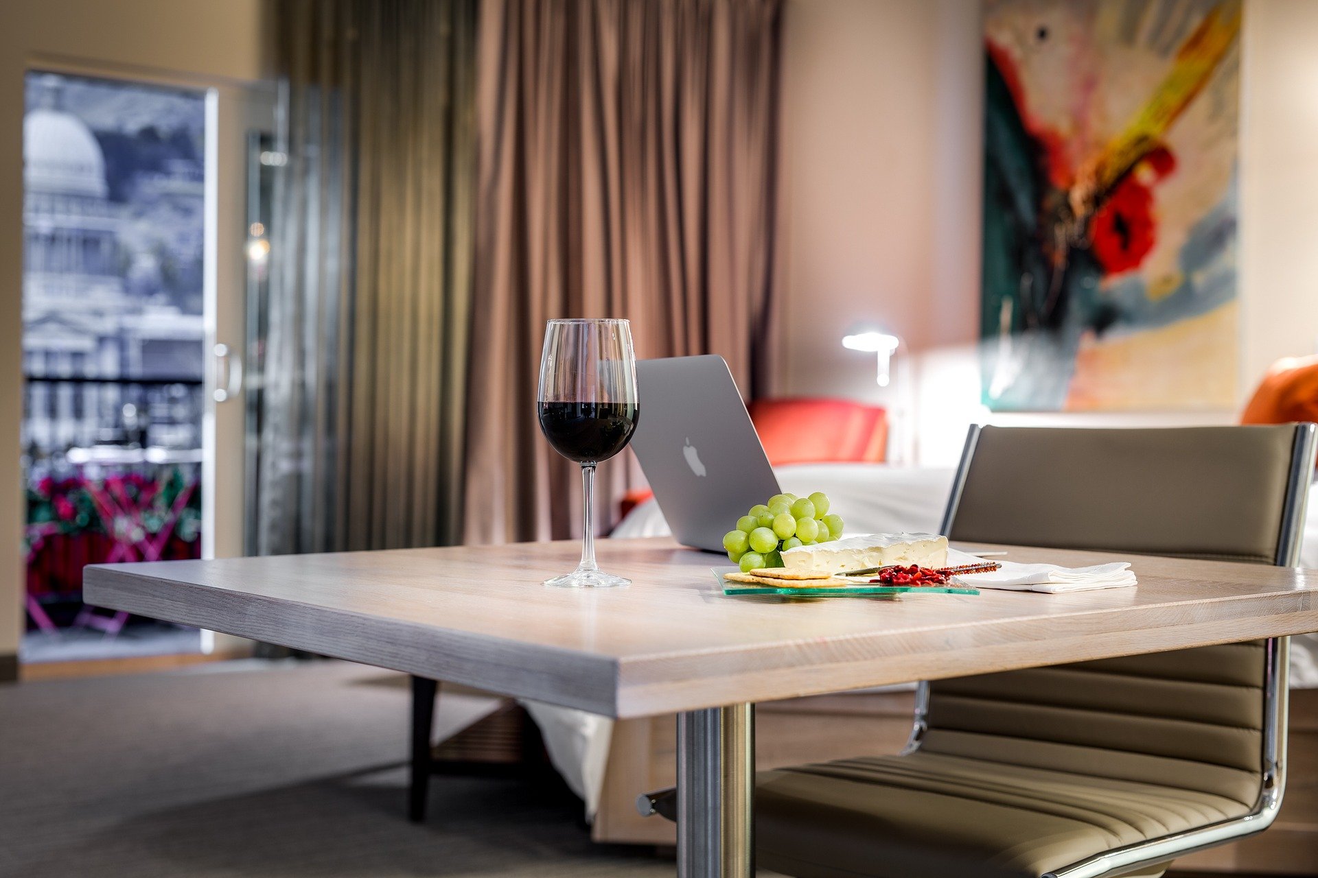 Hotel room with a table set up with a class of wine, cheese platter, and a laptop