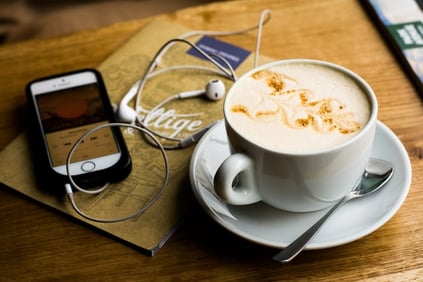 Handy mit Podcast neben einer Kaffeetasse
