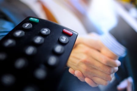 Close up of a TV remote with human hands in the background