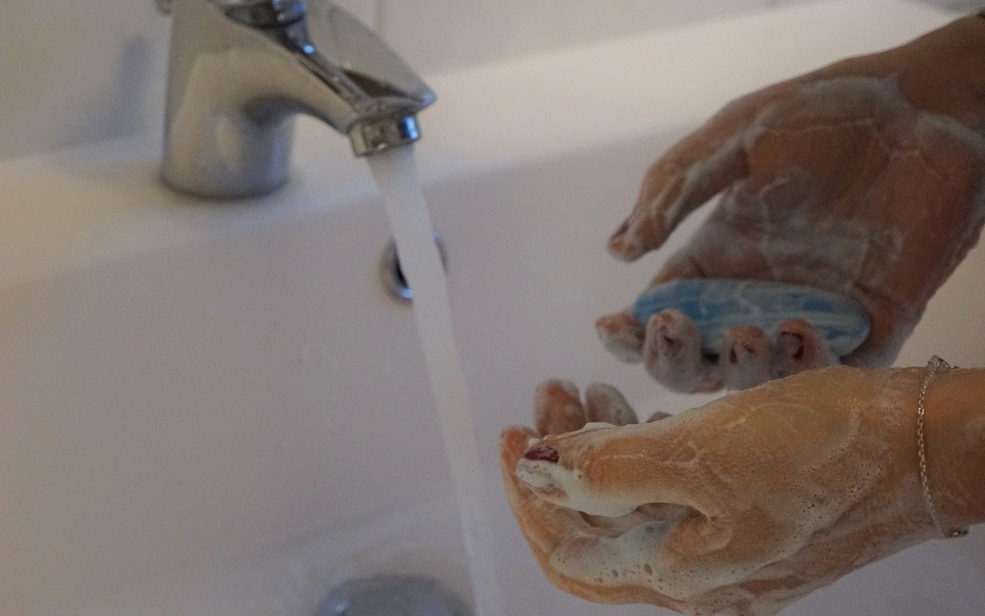 Lady washing hands with a bar of soap in a sink with a silver tap.